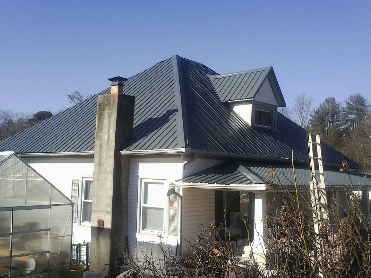Dark blue standing seam metal roof on a white farmhouse with dormer — Slate & Tile Roof Repair by Roofing Brothers in Northbridge