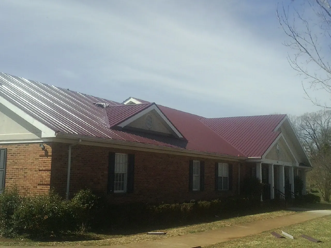 Red metal roof with gabled entries on a long brick building, from a Hail Damage Roof Repair job in Northbridge