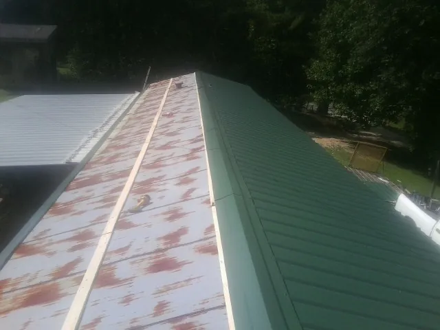 Old rusted panels beside newly installed green metal roofing — Wind Damage Roof Repair by Roofing Brothers in Northbridge