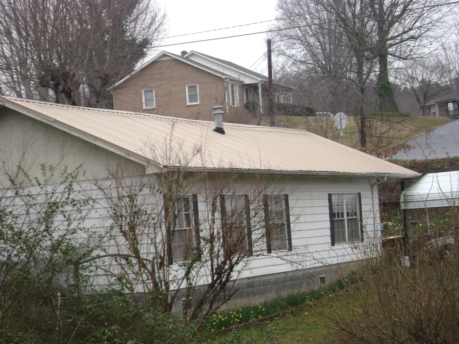 Tan metal roof on a white sided house set into a hillside — Commercial Roofing by Roofing Brothers in Northbridge