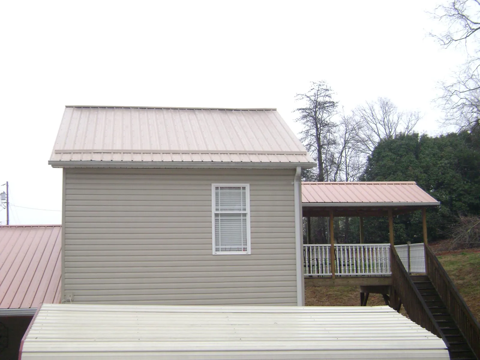 Tan metal roofs on a two story addition and attached porch, from a Roof Replacement job in Northbridge